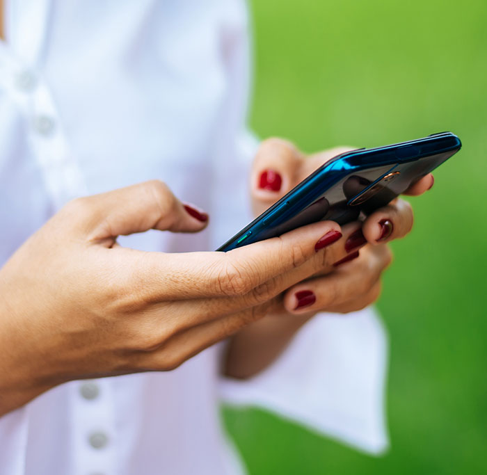 Woman with red nail polish holding a smartphone, symbolizing a woman who believes a friend and realizes she got duped.