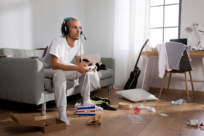 Young man playing video games in messy room after lady helps 23YO friend with a place to stay and a job