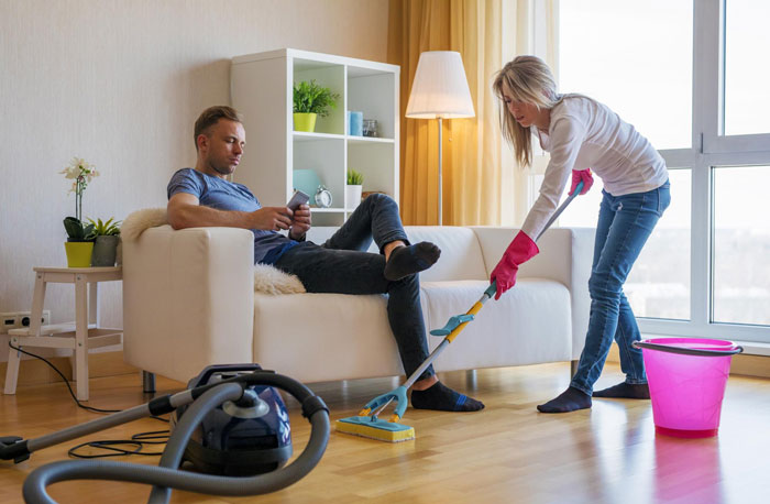 Woman helping 23-year-old friend with a place to stay and a job while he lounges on the couch using his phone.