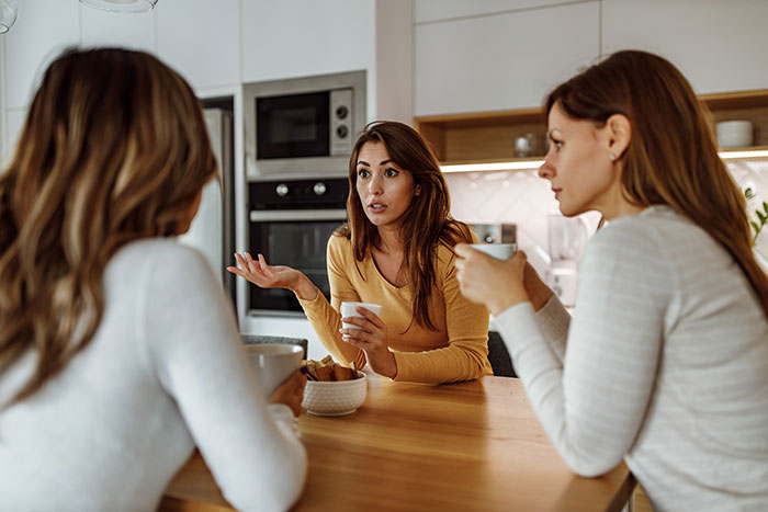 Three women discussing wedding plans in a modern kitchen, capturing a bride getting a reality check about elaborate weddings.