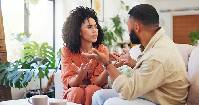 Woman and man having a serious conversation indoors, depicting a tense moment related to autistic child and work trip vacation.
