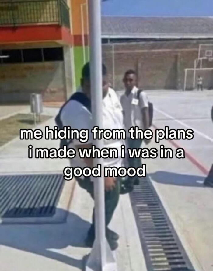 Person partially hidden behind a pole in a schoolyard representing relatable memes to help cope with anxiety.