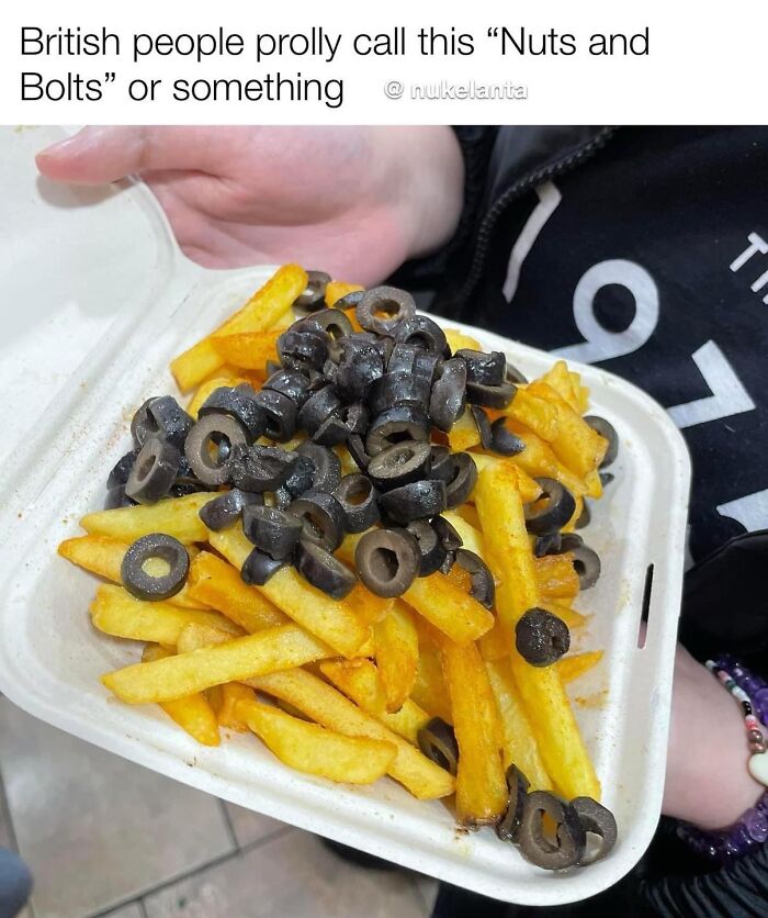 Close-up of fries topped with black olives held in a takeaway container, serving as a funny meme food joke.