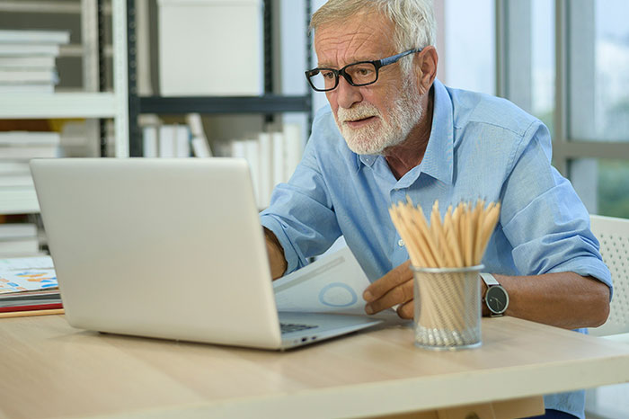 Older man struggling with technology, confused while using laptop, illustrating cluelessness with digital devices.