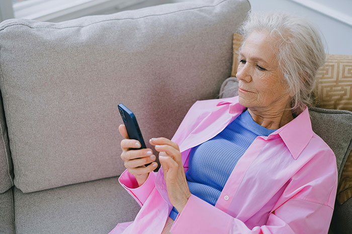 Older woman struggling with technology using smartphone on couch, illustrating cluelessness with tech among seniors.