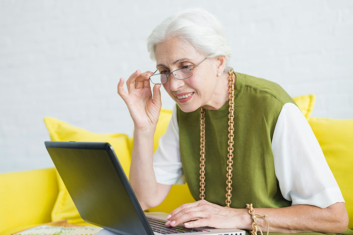 Older woman adjusting glasses while looking confused at laptop, illustrating older people clueless with technology online.