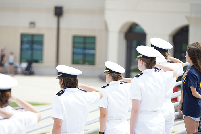 Older people struggling with technology, walking outdoors near a building while wearing white uniforms and hats.