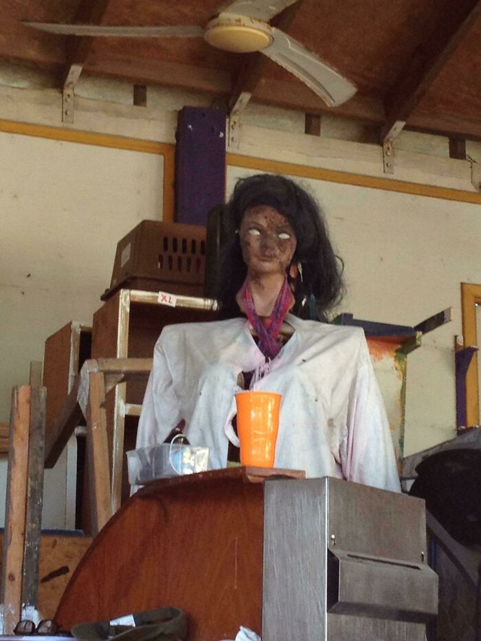 Creepy photo of a mannequin with white eyes and worn clothes in a cluttered room causing a spooky feeling.