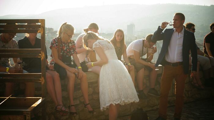 Group of young adults socializing outdoors at sunset, with some people enjoying drinks and sharing funny drunk fumbles moments.