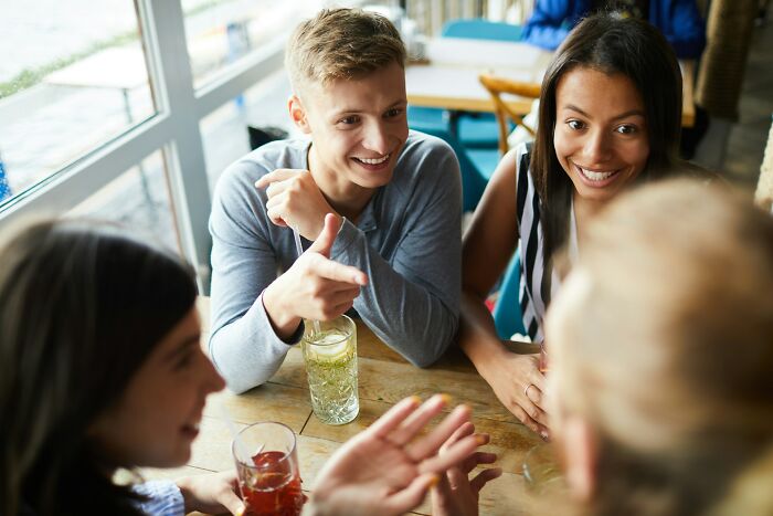 Group of young people socializing at a cafe, discussing relationship topics including cheating signs in women.