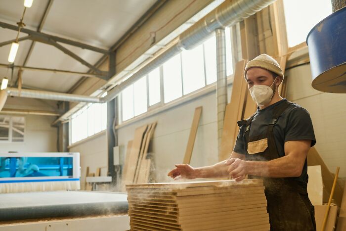 Carpenter wearing mask working with wood in workshop, illustrating a near-death experience with dust particles in the air.