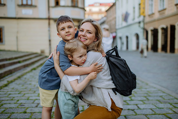 Woman suspects fianc&eacute; hiding a secret kid after finding kids' clothing, pictured hugging two children outdoors on a cobblestone street.