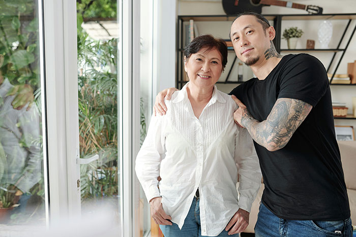 Young man with tattoos and his older female relative smiling indoors, representing financial favor and loan repayment concepts. Young man with tattoos and his older female relative smiling indoors, representing financial favor and loan repayment concepts.
