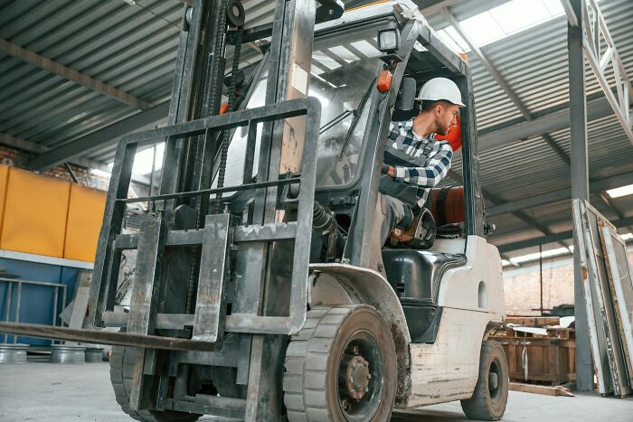 Man wearing a hard hat operating forklift inside industrial warehouse.