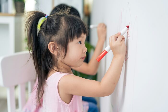 Young children drawing with markers on a wall during disastrous playdates parents wish they could forget.