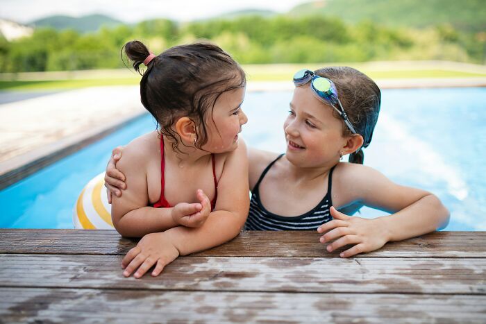 Two young girls sharing a playful moment in a pool during a memorable and disastrous playdate for parents.