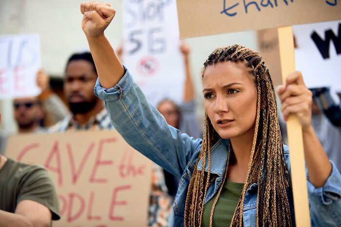 A determined woman with braided hair raises her fist at a protest against common untrue propaganda beliefs.