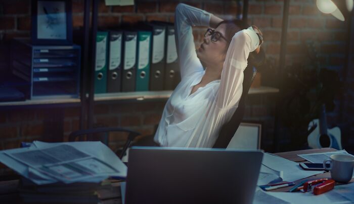 A stressed woman sitting at a cluttered desk late at night, reflecting on job loss due to AI impact.