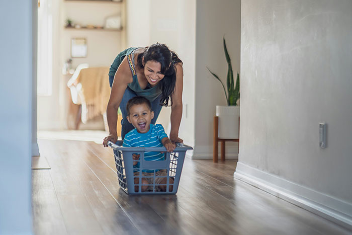 Young woman caring for toddler in laundry basket, illustrating mom abandonment and sibling caregiving themes.