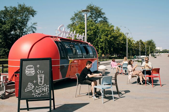 Outdoor restaurant seating with customers and a red food truck, illustrating tales from restaurant staff about unpaid bills.