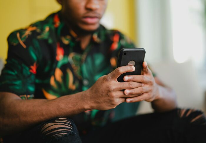 Young man with patterned shirt and ripped jeans focused on his phone sharing chaotic breakup stories.