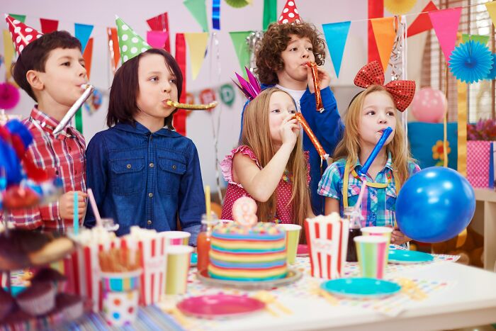 Children wearing party hats and blowing party blowers at a colorful playdate with festive decorations and snacks.