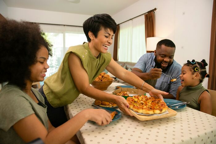 Family enjoying a lively playdate around a table with pizza, capturing memorable and unpredictable moments parents never forget.