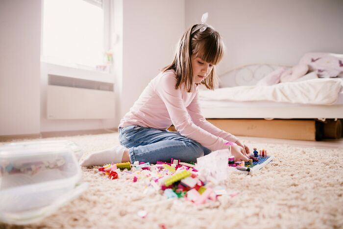 Young girl playing with colorful building blocks on carpet.