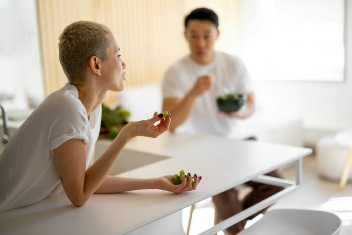 Woman and man eating in a modern kitchen, illustrating potential cheating signs in women shared by broken-hearted men.