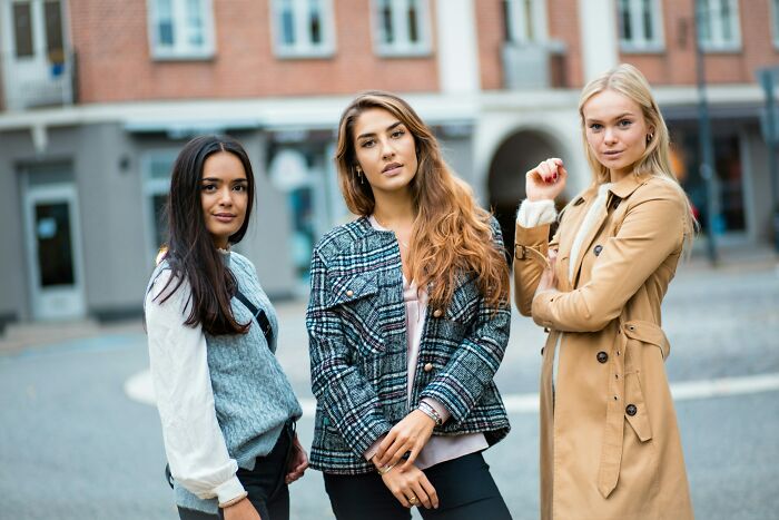 Three confident women standing outdoors in stylish clothes, representing positive stereotypes about various countries.
