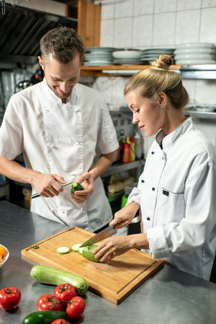 Two chefs in white uniforms slicing vegetables in a kitchen, illustrating stories of karma striking with zero mercy.