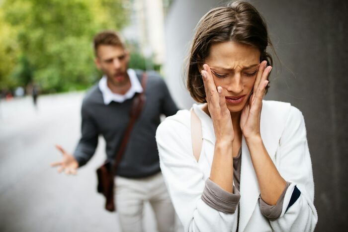 Woman showing signs of distress while a man angrily gestures behind her, illustrating cheating signs in women.
