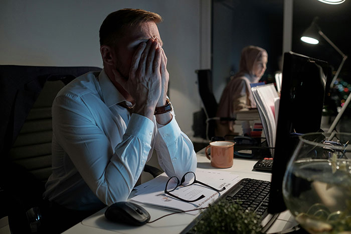 Man in office wearing white shirt, stressed and covering face, dealing with younger coworker flirt late at night. Man in office wearing white shirt, stressed and covering face, dealing with younger coworker flirt late at night.