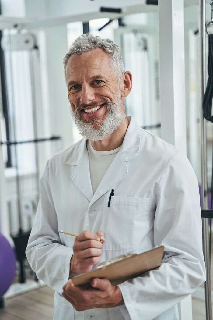 Smiling male health professional in a white coat holding a clipboard in a gym setting promoting healthy habits.