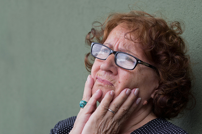 Concerned older woman with glasses touching her face, reflecting on issues with absentee husband wanting third child.