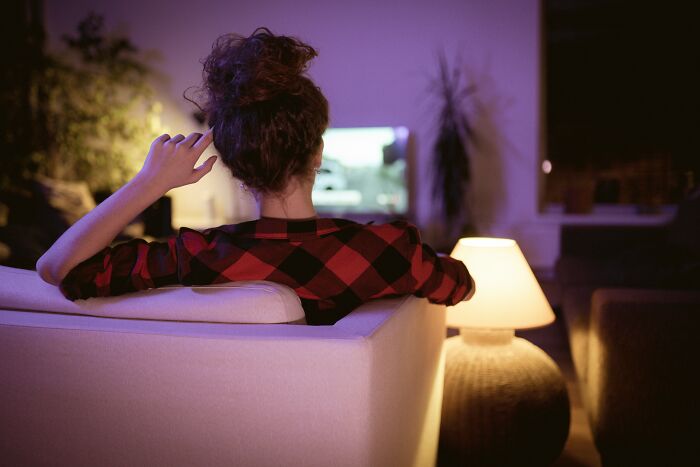 Woman in a red plaid shirt sitting on a couch at night, watching TV alone, creating a creepy and unexplainable atmosphere.