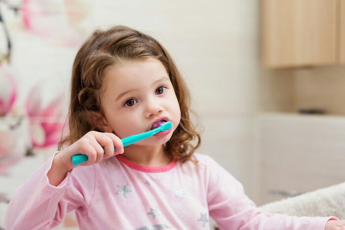 Young girl brushing teeth in bathroom, representing medical neglect effects on daily health routines.