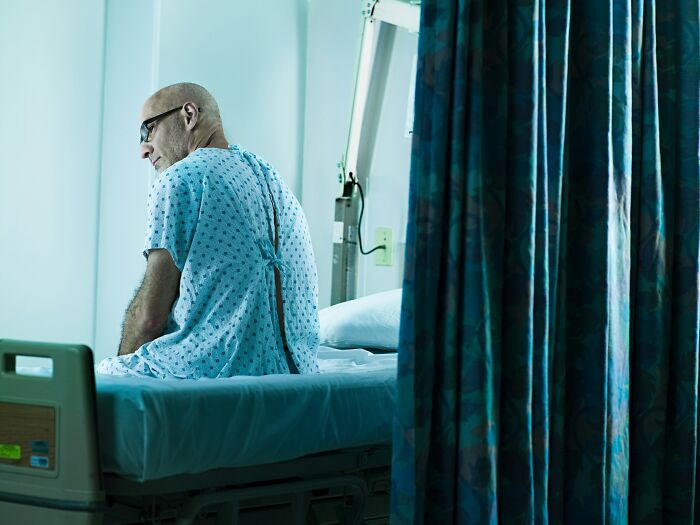 Patient in hospital gown sitting on bed at night, evoking scary ghost stories related to hospital work atmosphere.