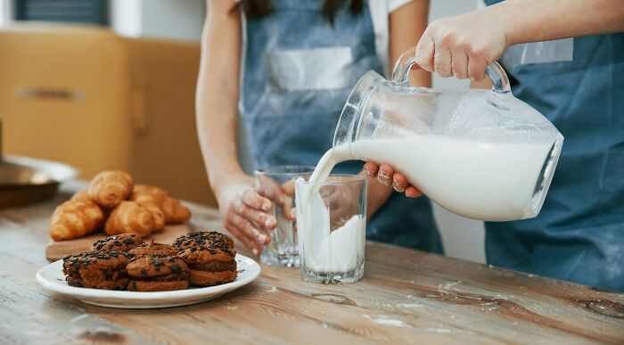 Person pouring milk into a glass with cookies and croissants on a wooden table illustrating common truths and propaganda.
