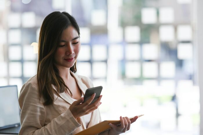 Woman holding a smartphone and notepad, learning simple car stuff skills with minimal training for maximum results.