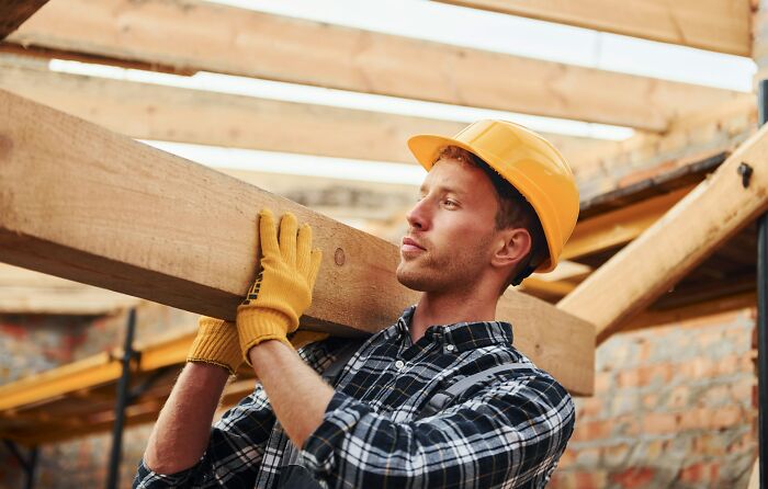 Man in a yellow hard hat carrying a wooden beam, demonstrating simple car stuff skills for effective results.