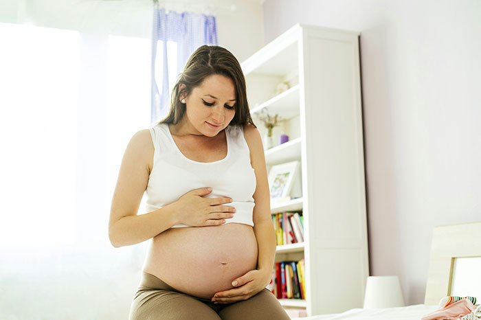 Pregnant woman gently holding belly in a bright room, reflecting on naming baby after childhood dog Lassie.