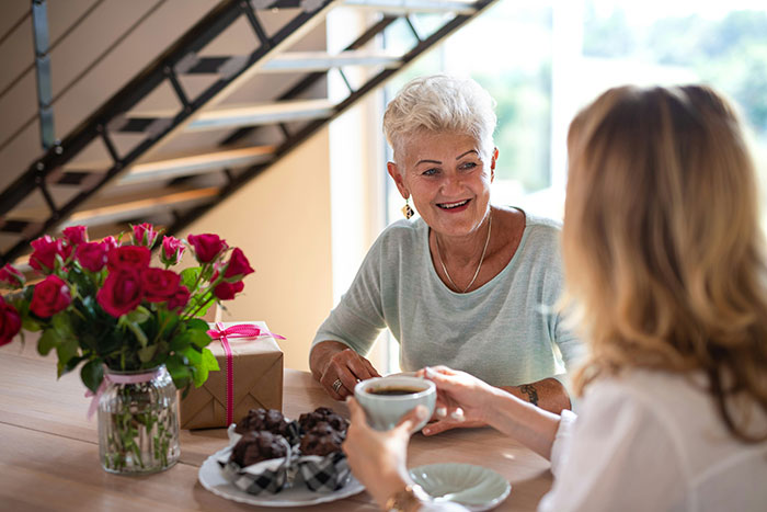 Elderly grandma smiling at woman during coffee, highlighting family care and refusal to take responsibility challenges.