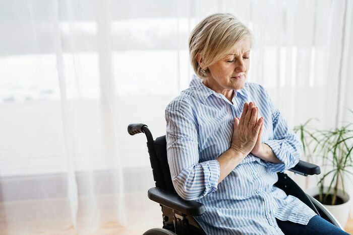 Elderly woman in wheelchair with hands clasped, reflecting on experiences of rude and ableist treatment faced by people with disabilities.