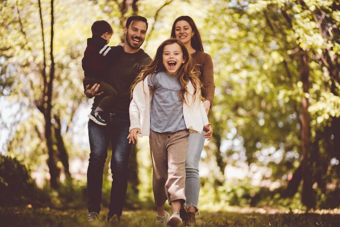 Happy family walking outdoors in a sunlit forest, highlighting emotional struggles and wife pondering ditching husband for good.