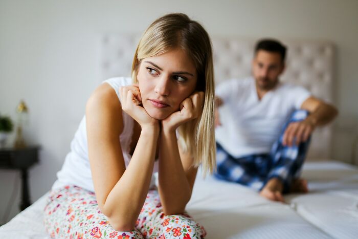 Young woman looking upset and distant on bed, illustrating common cheating signs in women observed by broken-hearted men.