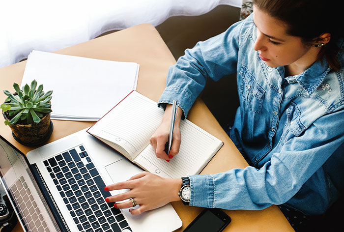 Woman writing in a notebook beside laptop, symbolizing woman ending her 2-year relationship after birthday cruise plans. Woman writing in a notebook beside laptop, symbolizing woman ending her 2-year relationship after birthday cruise plans.