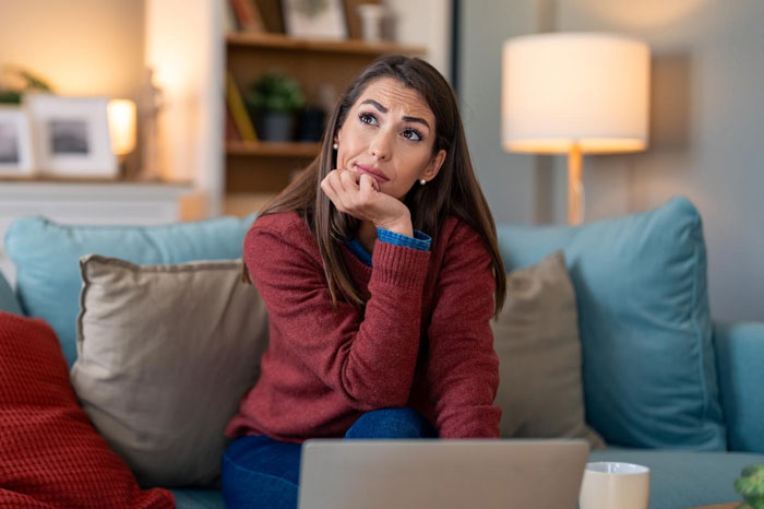 Woman sitting on couch looking thoughtful, representing a self-appointed fraud police scenario at a store.