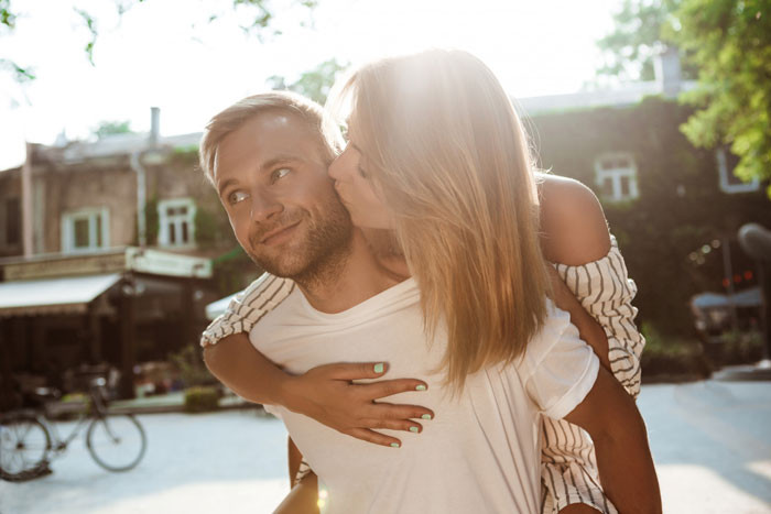 Woman proudly funding her stay-at-home boyfriend&rsquo;s life, showing affection outdoors on a sunny day.
