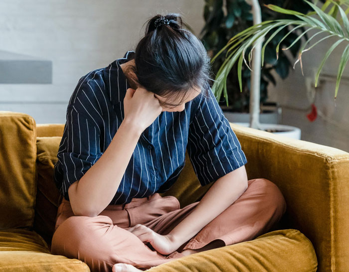 Woman sitting on couch looking upset, reflecting on boyfriend going on trip with female friend and relationship concerns.